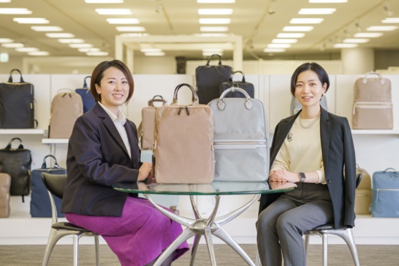 ファッションに合わせてお仕事リュックを活用すべき、と話す小林さんと森川さん。テーブルの上のバッグ左：スリファム、右：リモフィス