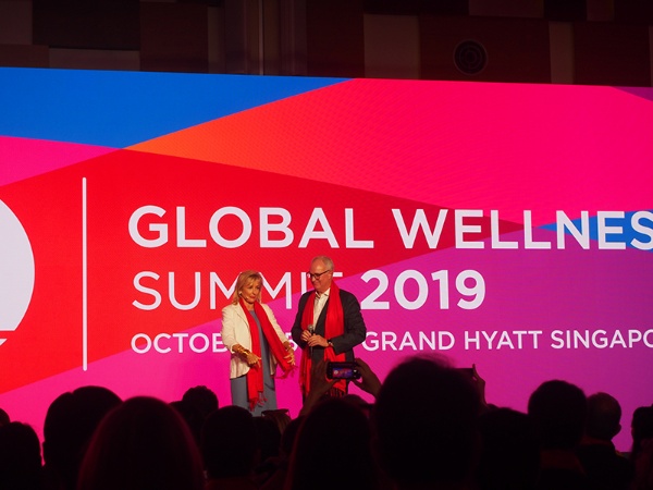 Global Wellness Summit（GWS）2019 in Singaporeの開会式。世界約150カ国のウェルネス業界から、500人以上もの参加者が集った。今年のテーマカラーは幸運、情熱を意味する「赤」ということで、参加者全員に赤いストールが配られ身に付ける。GWSの会長兼CEOのスージー・エリス（左）が開会宣言をした。