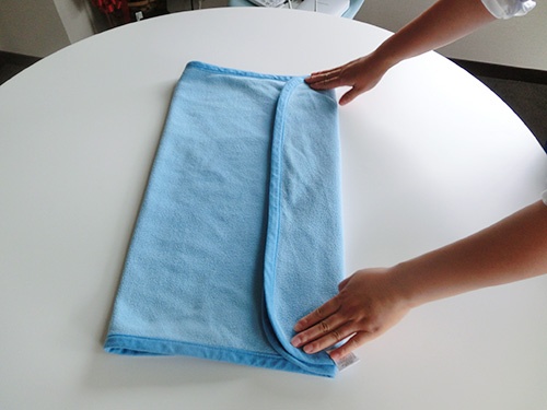 タオルを広げて２つ折りにし、下の端を3分の1ほど折り返します。