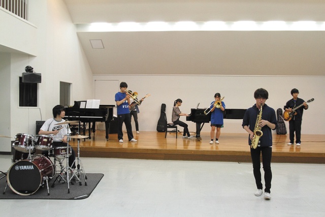 放課後にスタジオで演奏をする高校ジャズ部の生徒たち。男女が仲良く、声を掛け合いながら練習に励んでいる