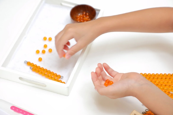モンテッソーリの感覚教具のひとつ、「ビーズ棒」。鮮やかなオレンジの珠を10集め、1本の棒にしていく過程で、子ども達は「長さ」で数の単位を覚えていきます